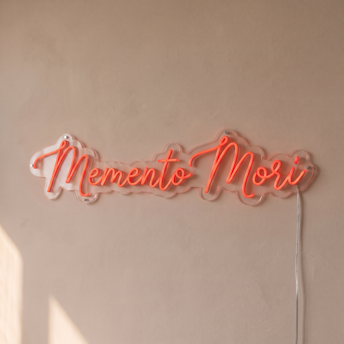 Gros plan du néon mural « Memento Mori » sur fond beige, tube allumé