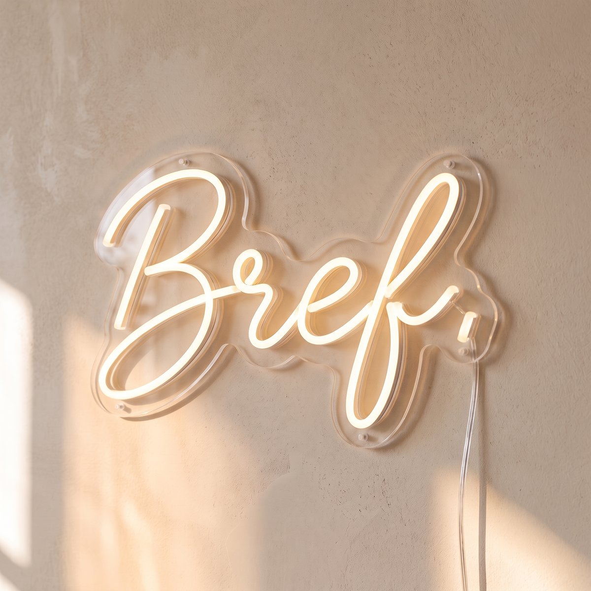 Gros plan du néon mural « Bref. » sur fond beige, tube allumé et support acrylique transparent