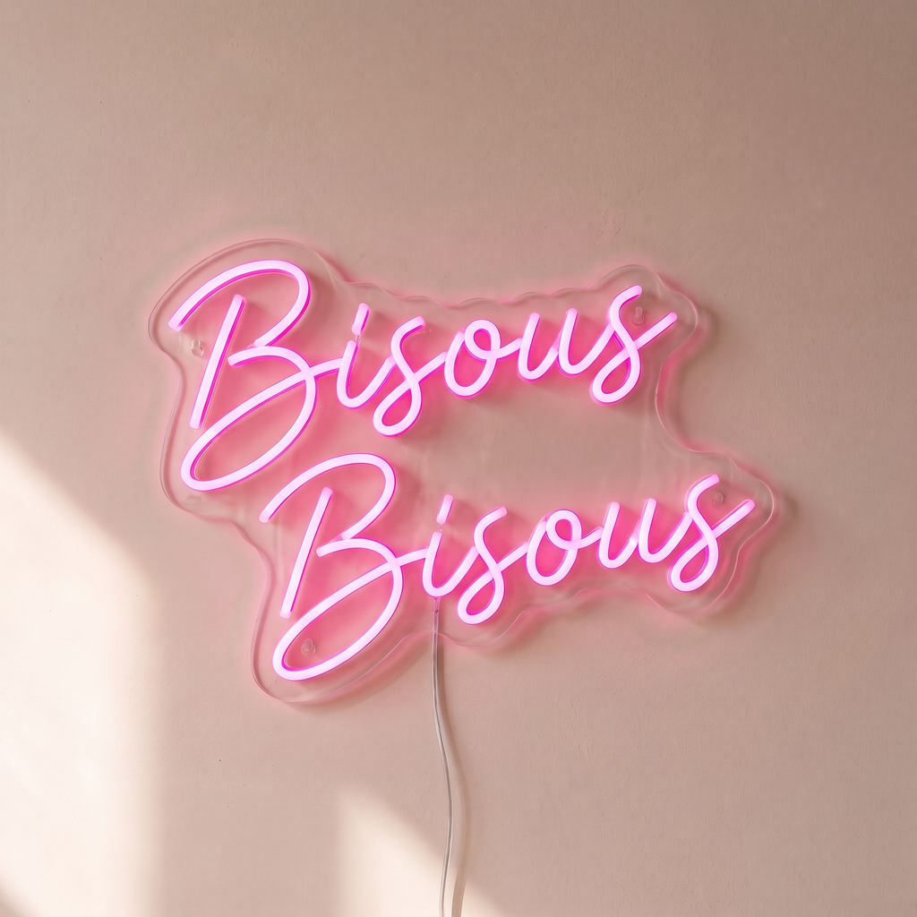 Gros plan du néon mural « Bisous Bisous » sur fond beige, tube allumé