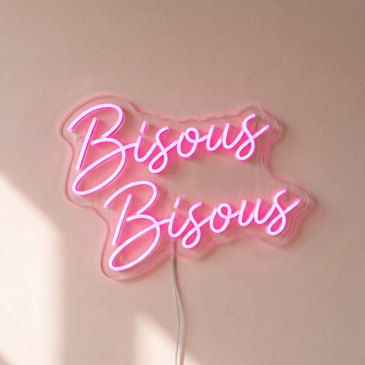 Gros plan du néon mural « Bisous Bisous » sur fond beige, tube allumé