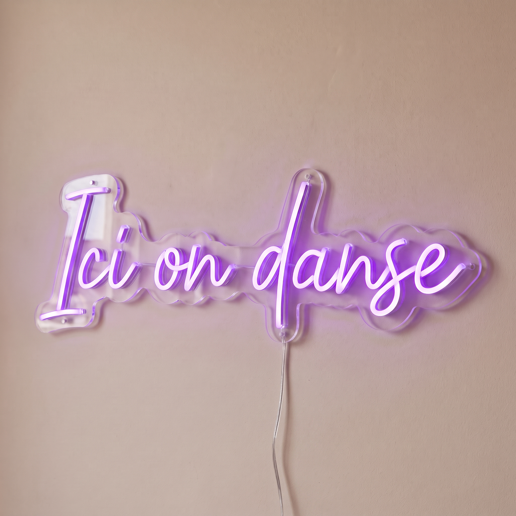 Gros plan du néon mural « Ici on danse » sur fond beige, tube allumé