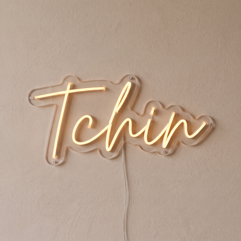 Gros plan du néon mural « Tchin » sur fond beige, tube allumé