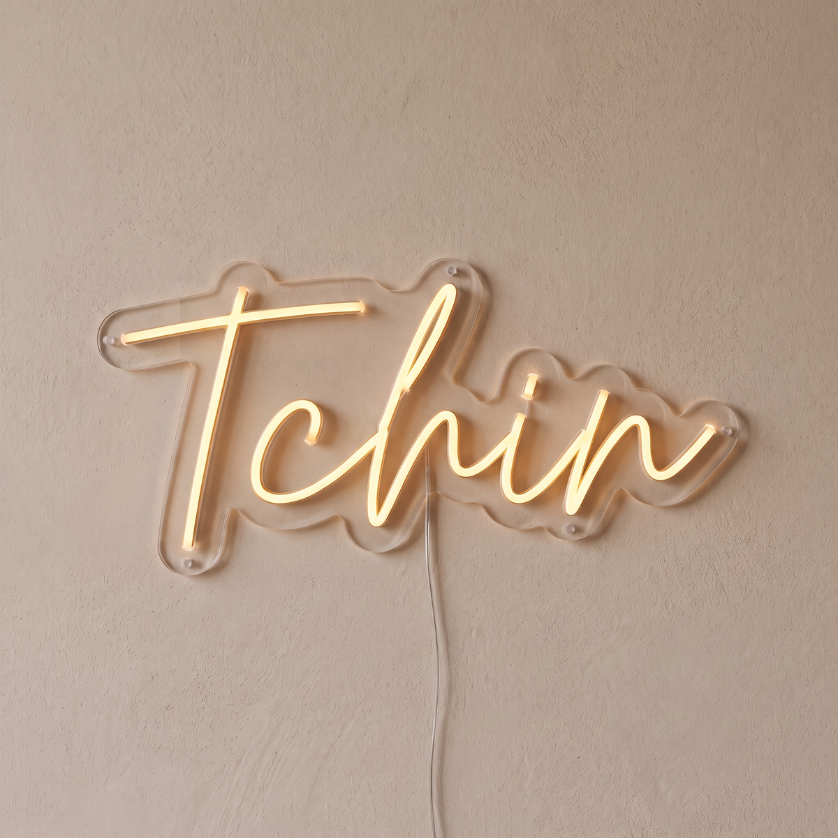 Gros plan du néon mural « Tchin » sur fond beige, tube allumé