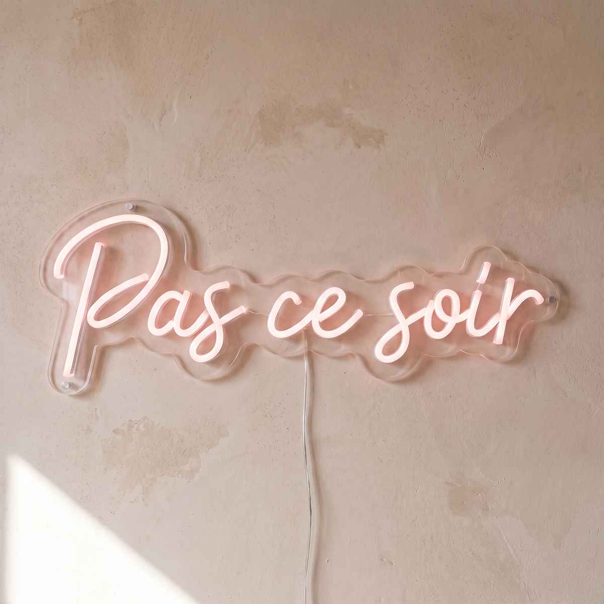 Gros plan du néon mural « Pas ce soir » sur fond beige, tube allumé