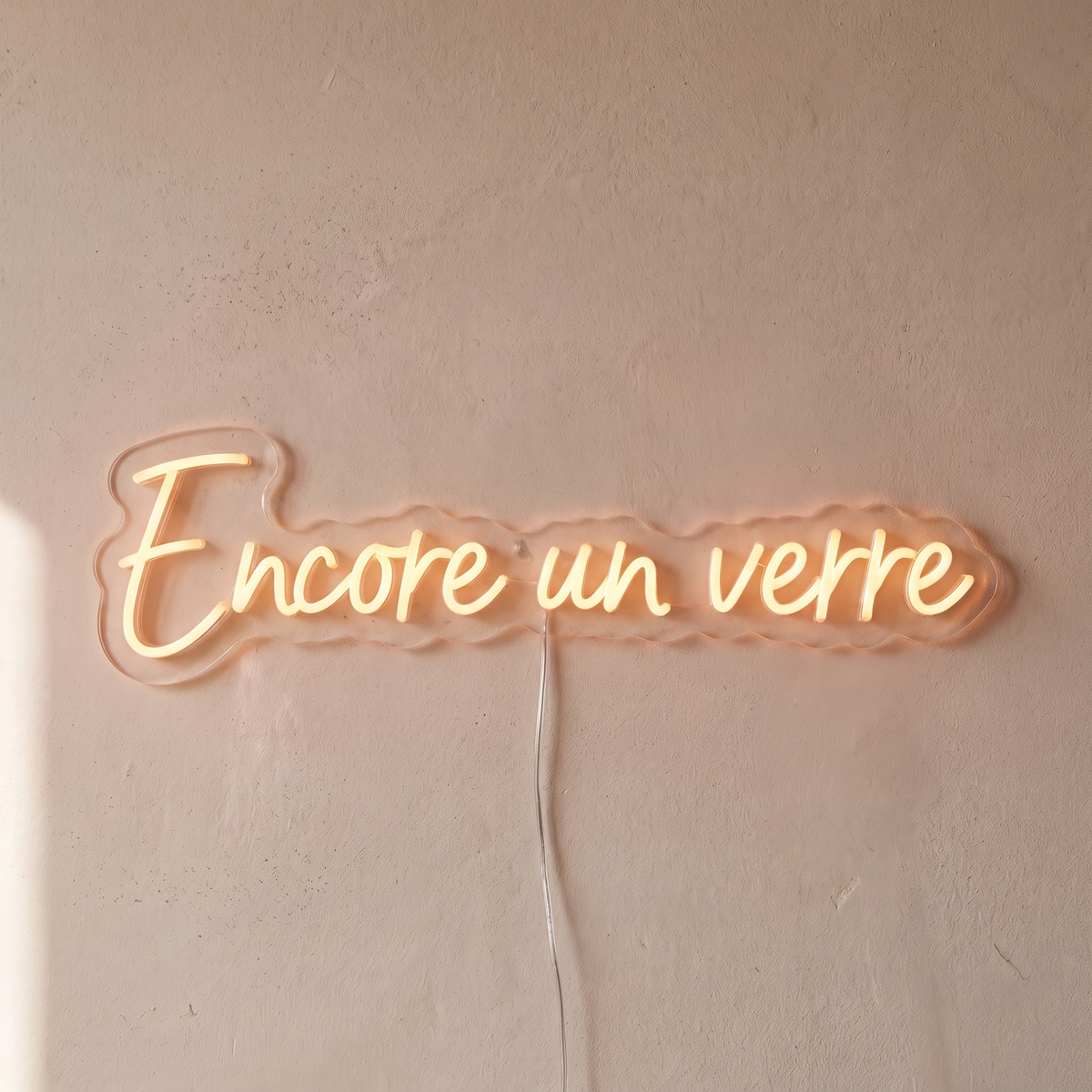 Gros plan du néon mural « Encore un verre » sur fond beige, tube allumé