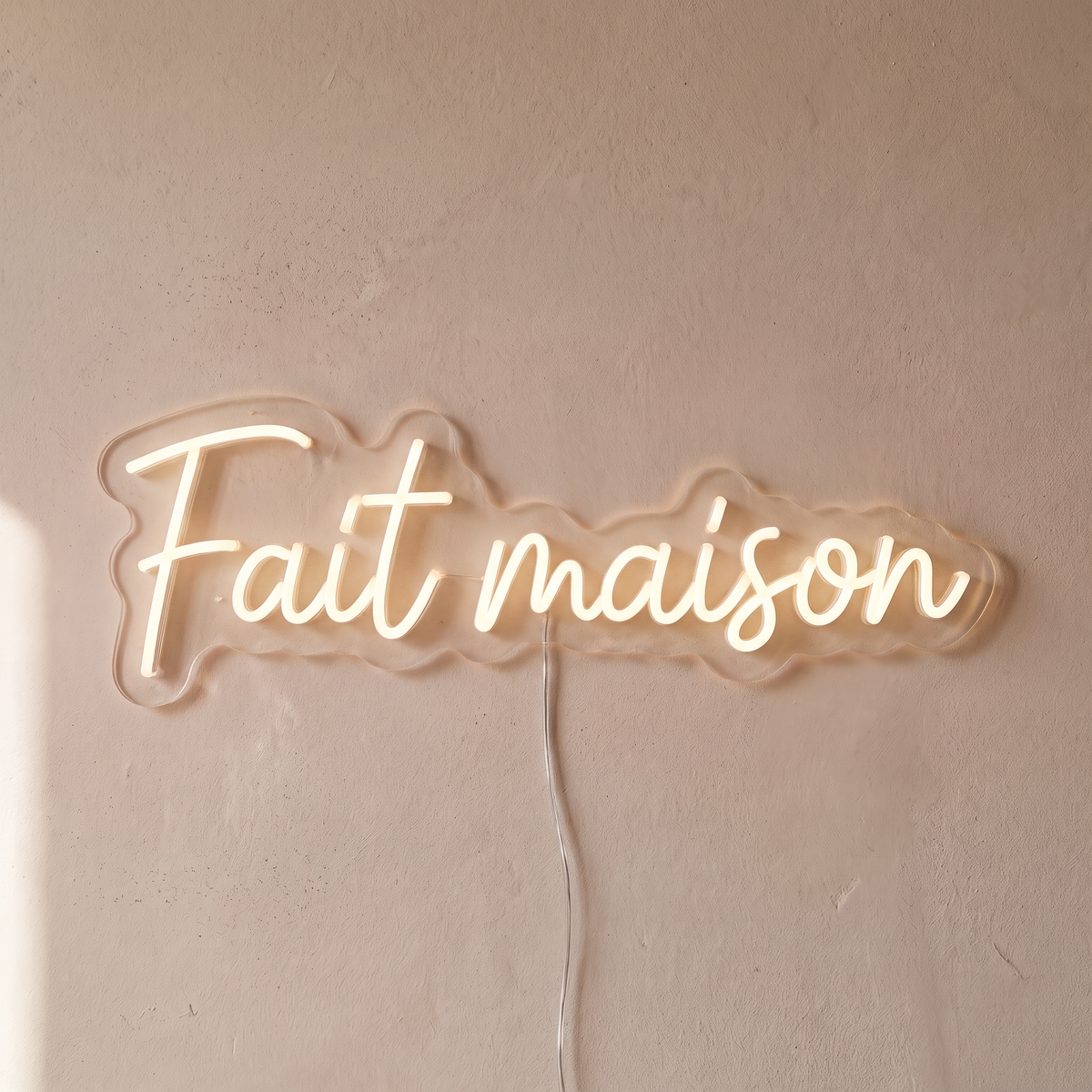 Gros plan du néon mural « Fait maison » sur fond beige, tube allumé