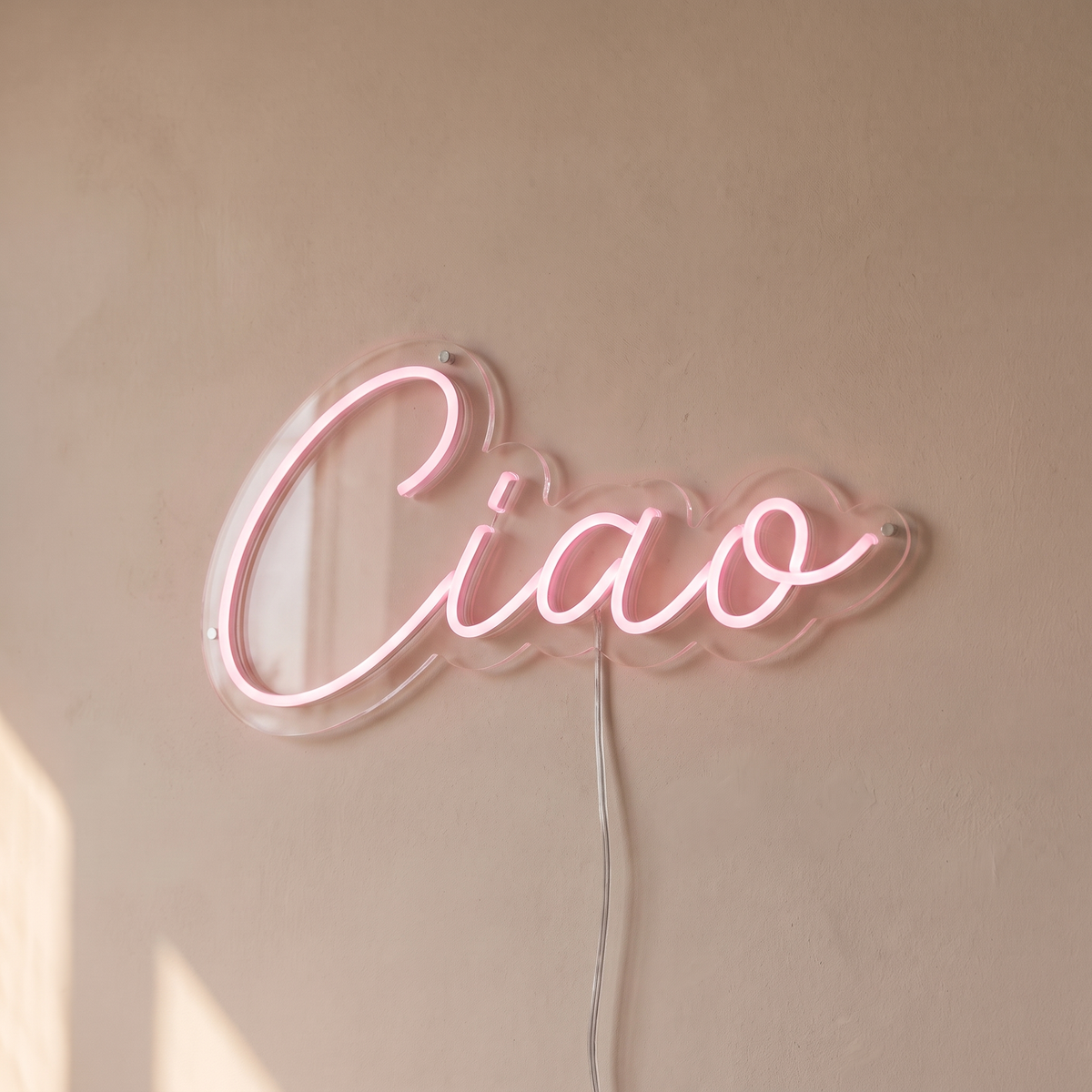 Gros plan du néon mural « Ciao » sur fond beige, tube allumé