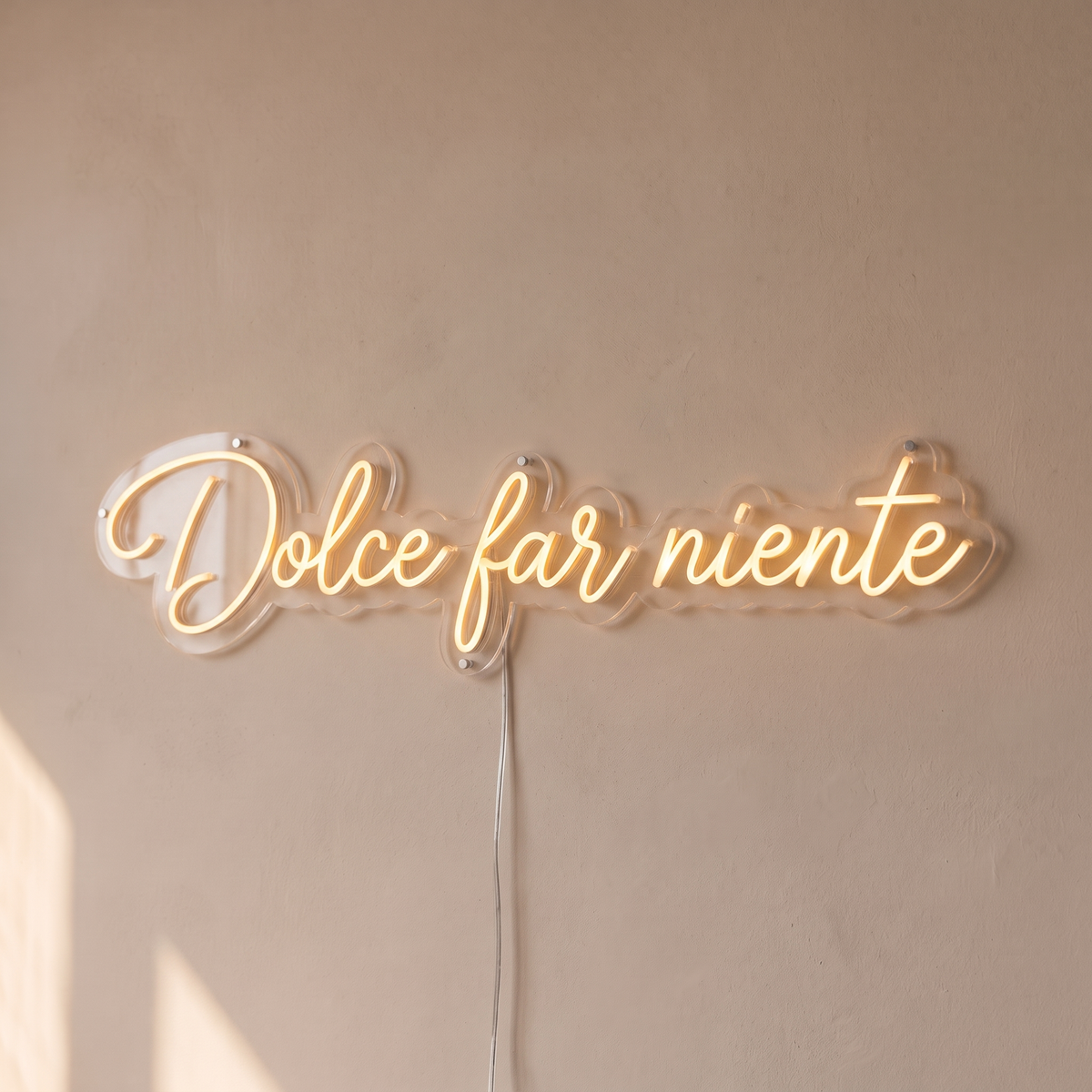 Gros plan du néon mural « Dolce far niente » sur fond beige, tube allumé
