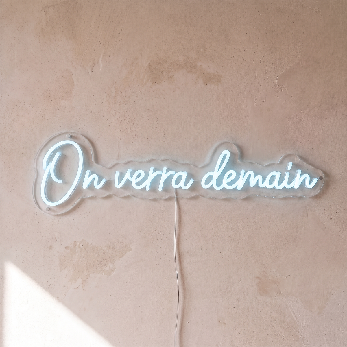 Gros plan du néon mural « On verra demain » sur fond beige, tube allumé