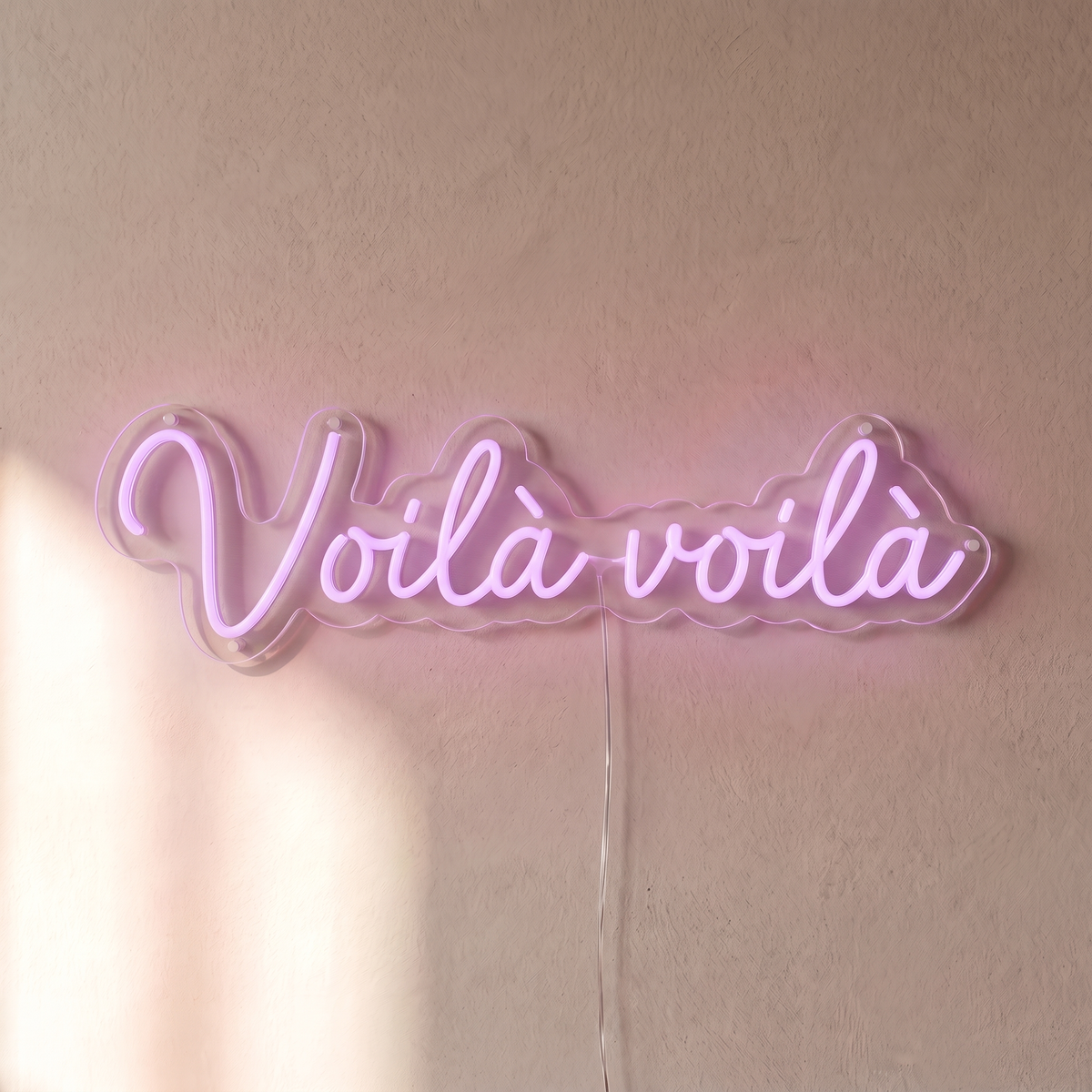Gros plan du néon mural « Voilà voilà » sur fond beige, tube allumé