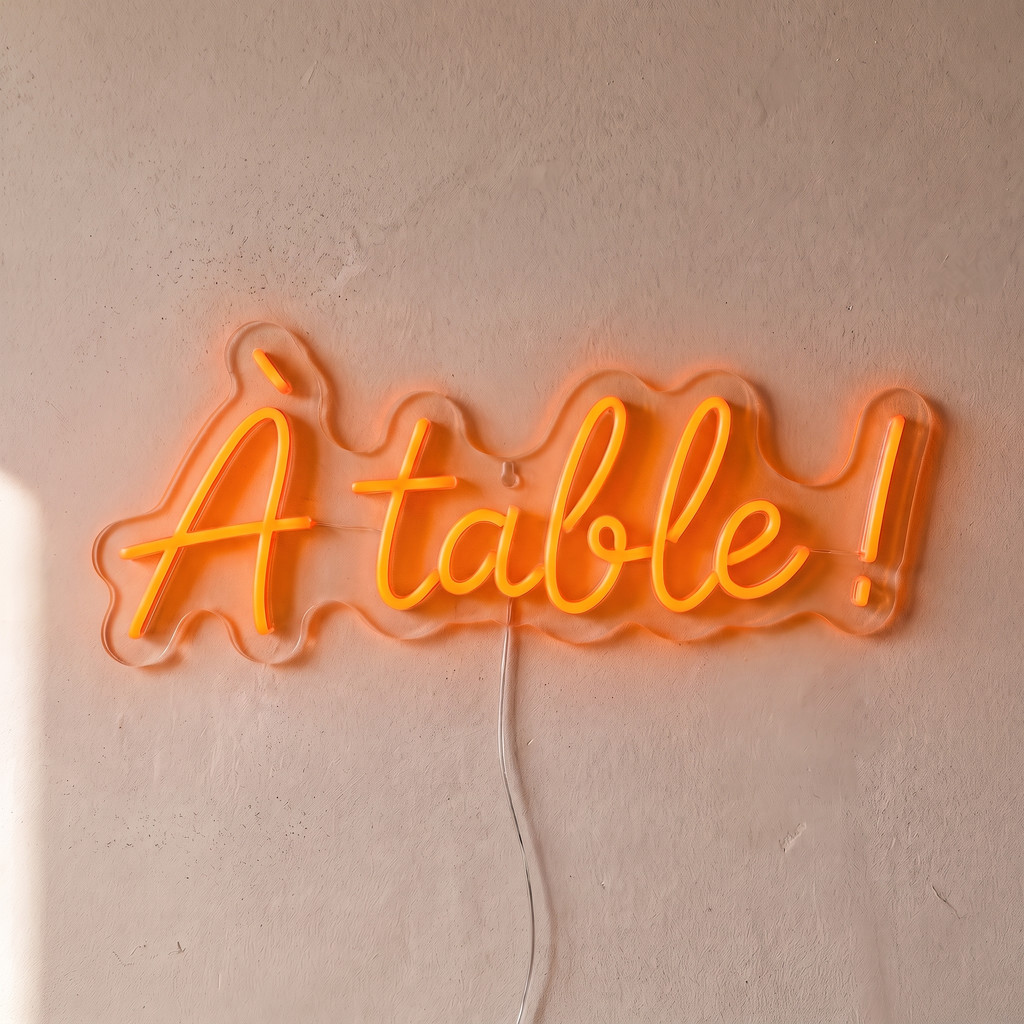 Néon mural « À table ! » orange, gros plan sur fond beige