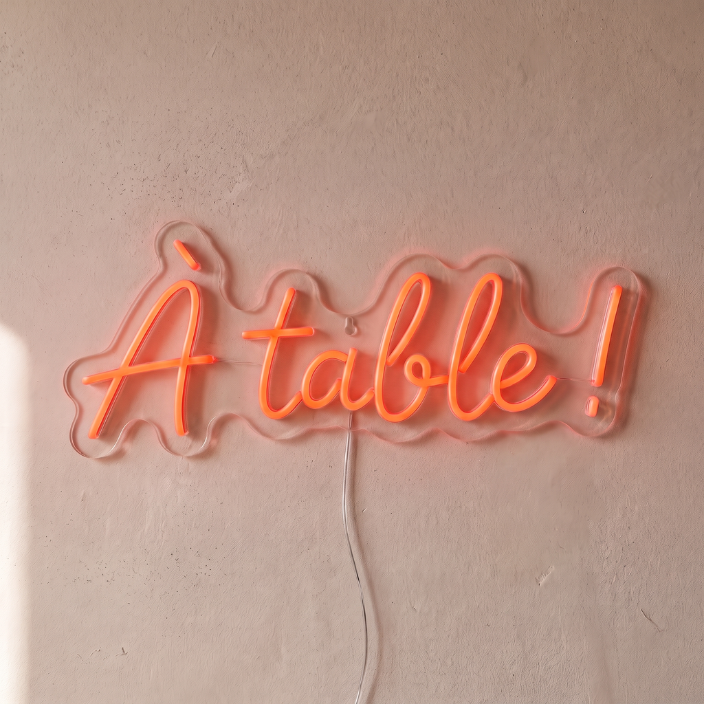Néon mural « À table ! » rouge orangé, gros plan sur fond beige