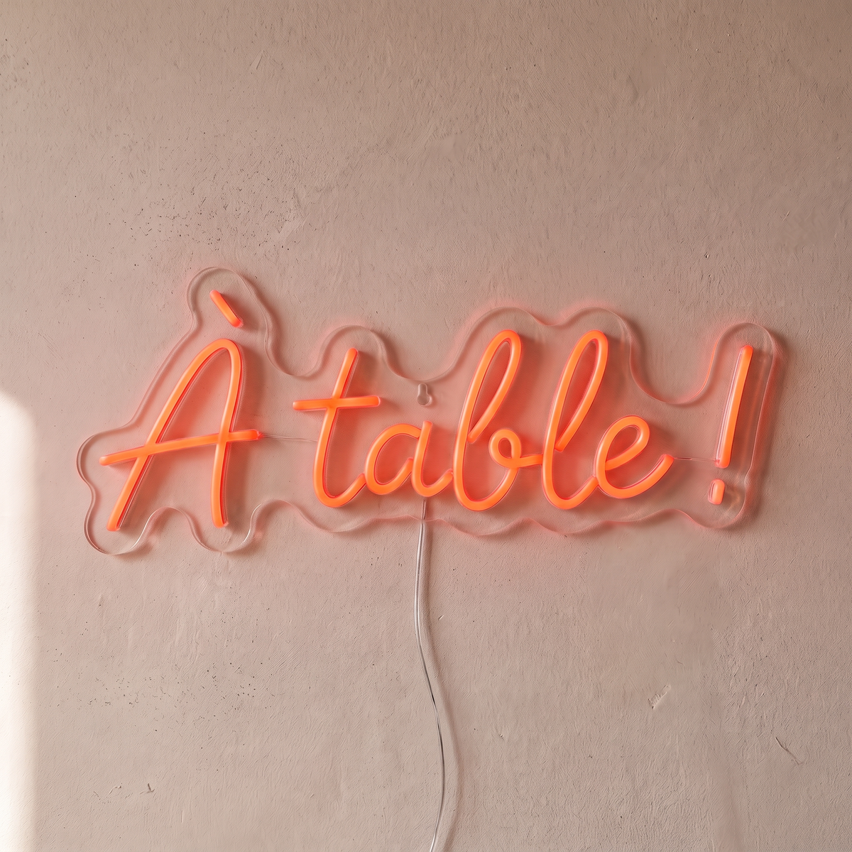 Néon mural « À table ! » rouge orangé, gros plan sur fond beige
