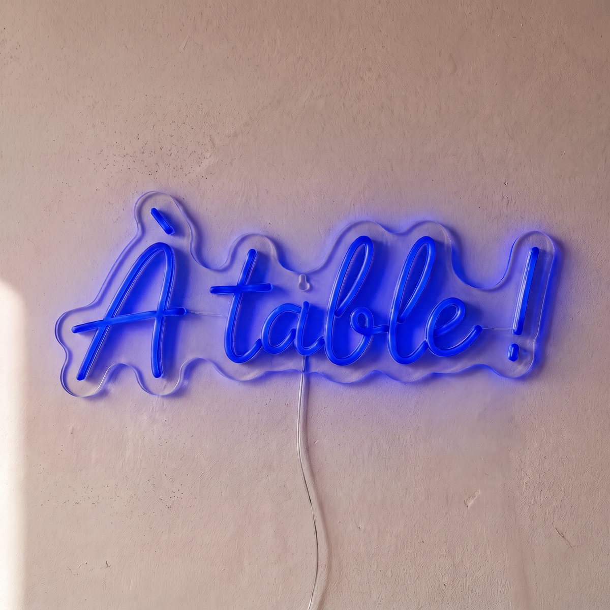 Néon mural « À table ! » bleu, gros plan sur fond beige