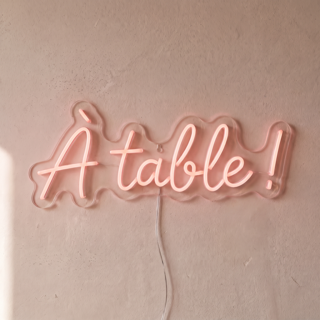 Néon mural « À table ! » rose pâle, gros plan sur fond beige