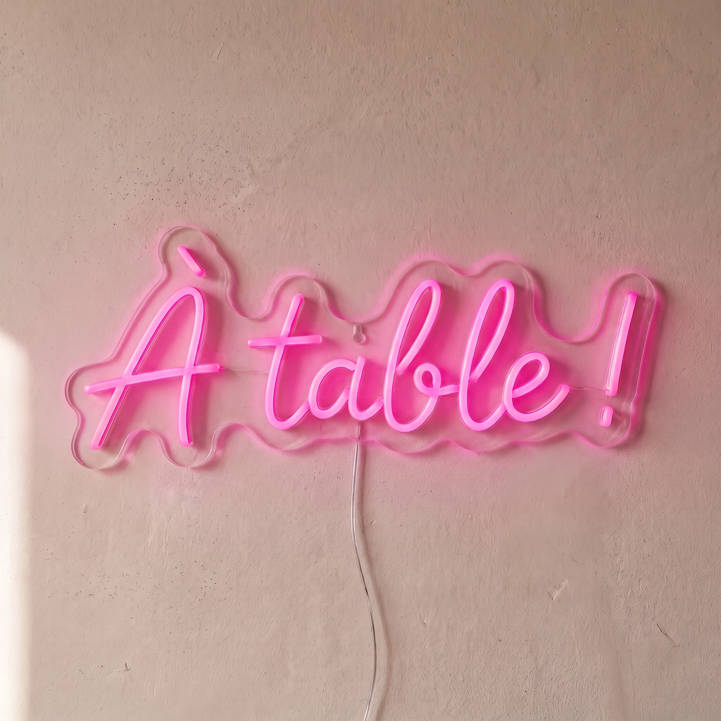 Néon mural « À table ! » rose, gros plan sur fond beige
