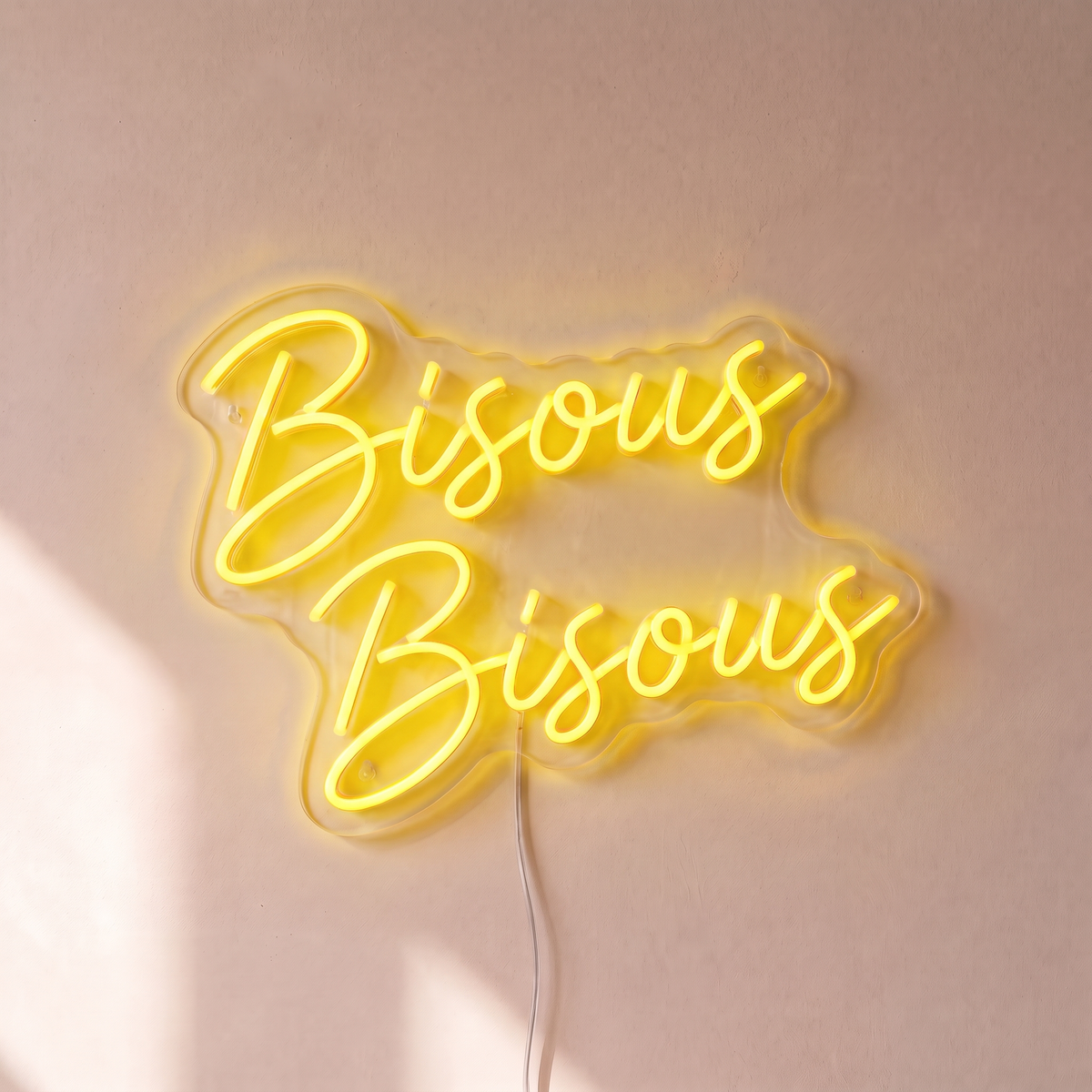 Néon mural « Bisous Bisous » jaune, gros plan sur fond beige
