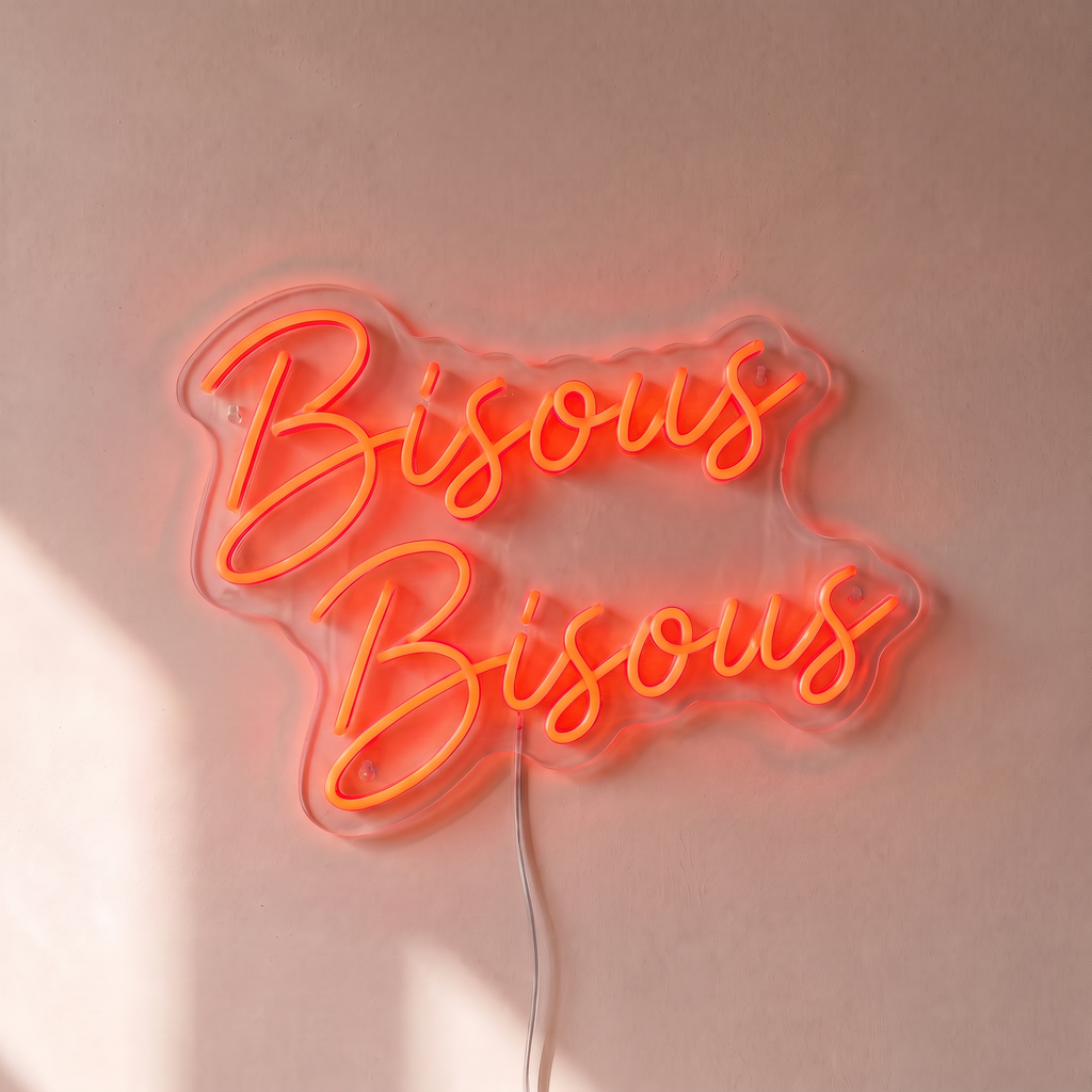 Néon mural « Bisous Bisous » rouge orangé, gros plan sur fond beige