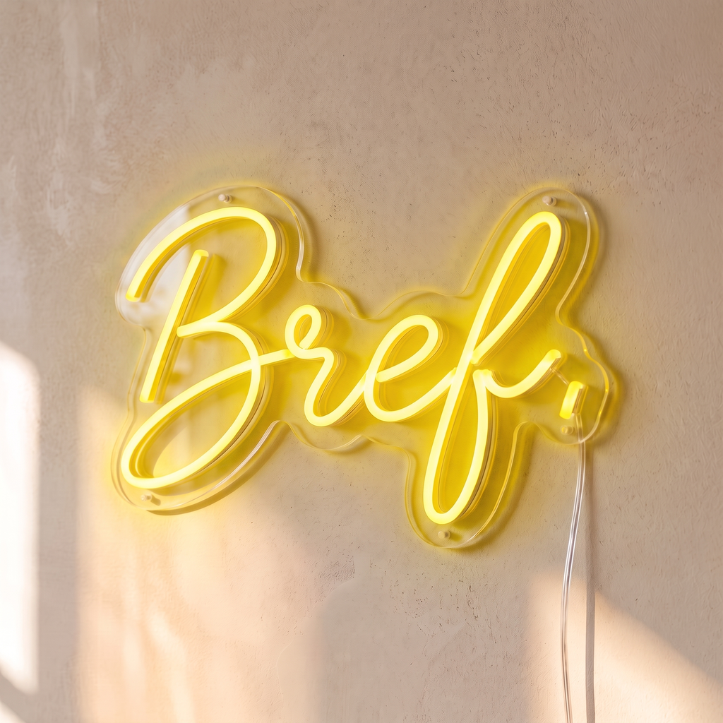 Néon mural « Bref. » jaune, gros plan sur fond beige
