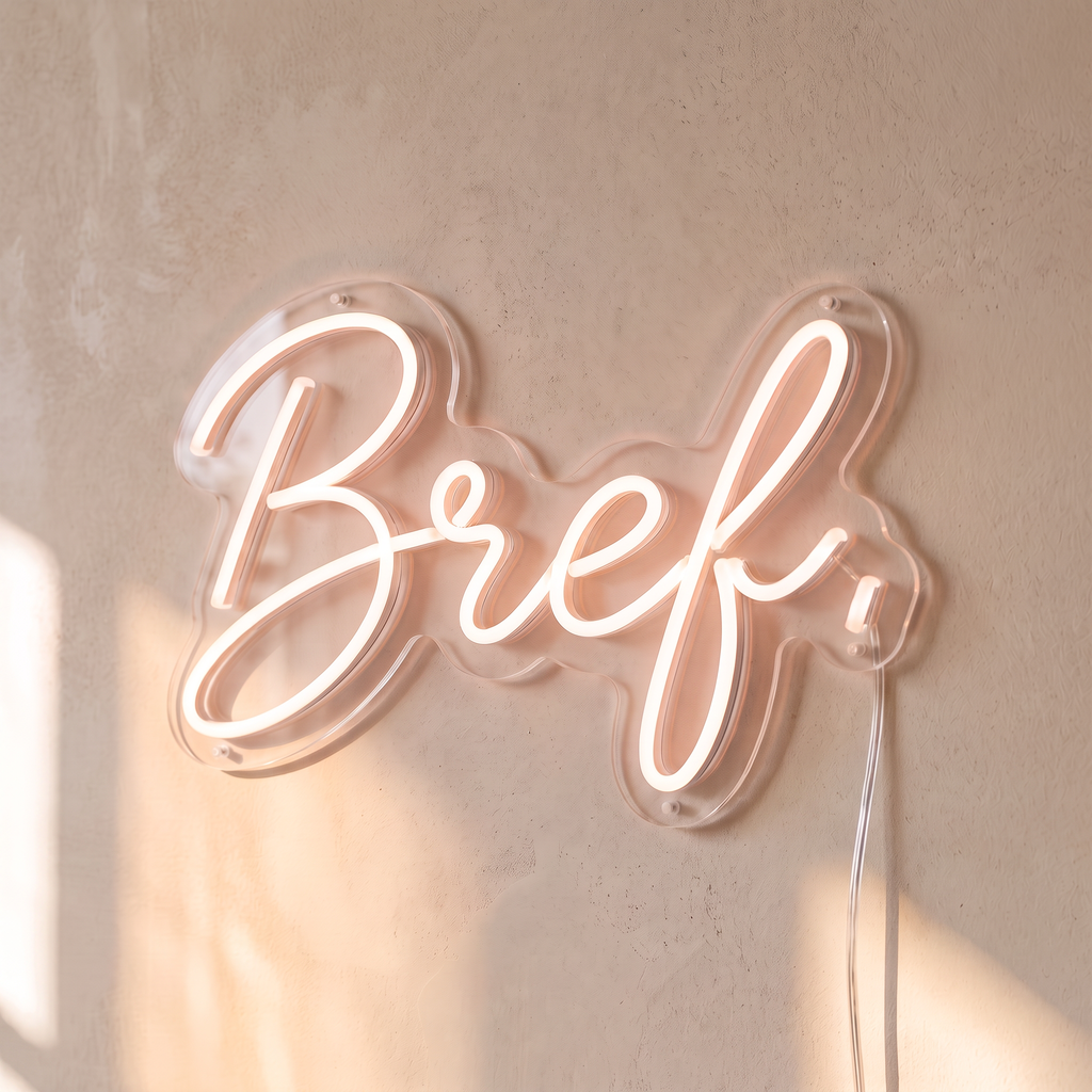 Néon mural « Bref. » rose pâle, gros plan sur fond beige