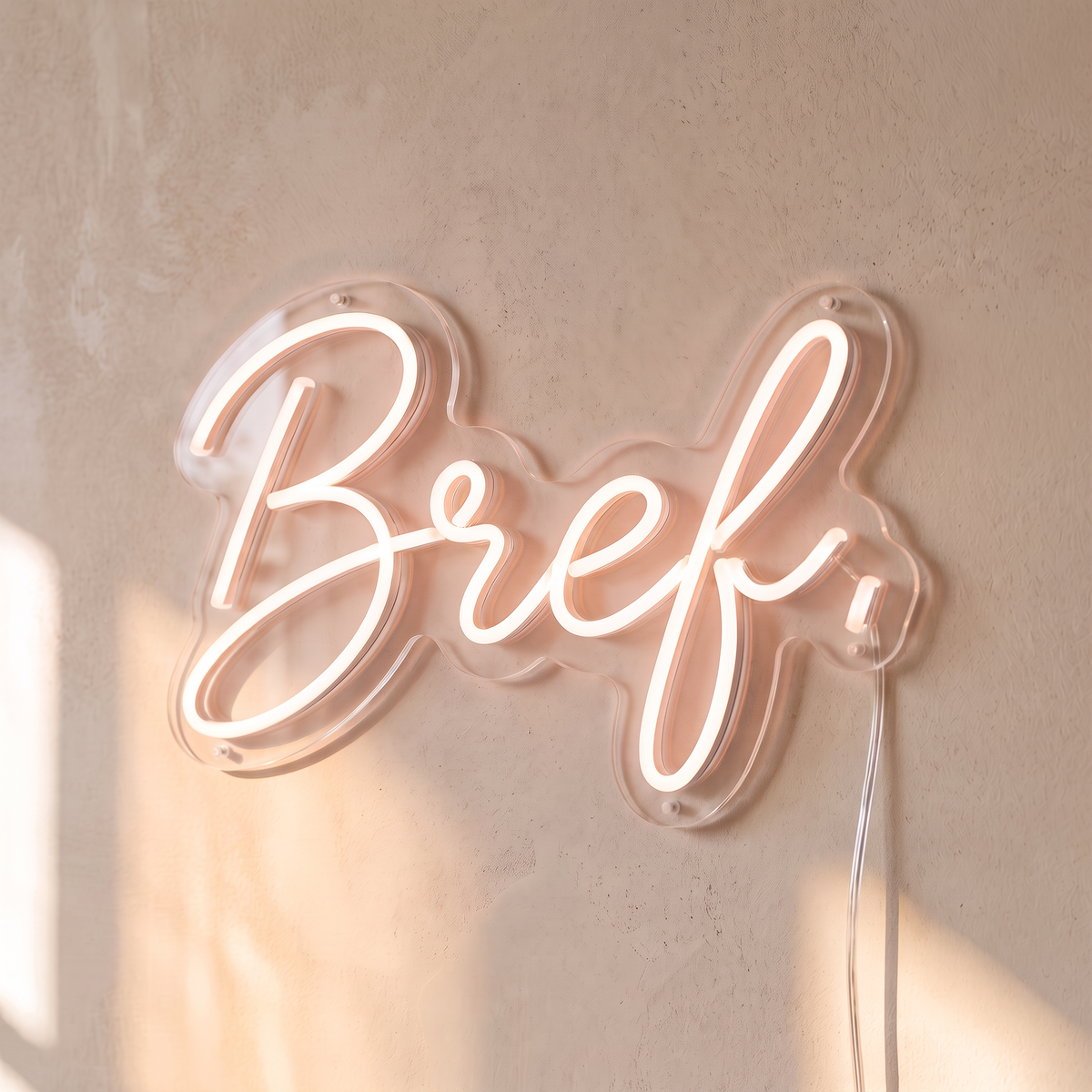 Néon mural « Bref. » rose pâle, gros plan sur fond beige