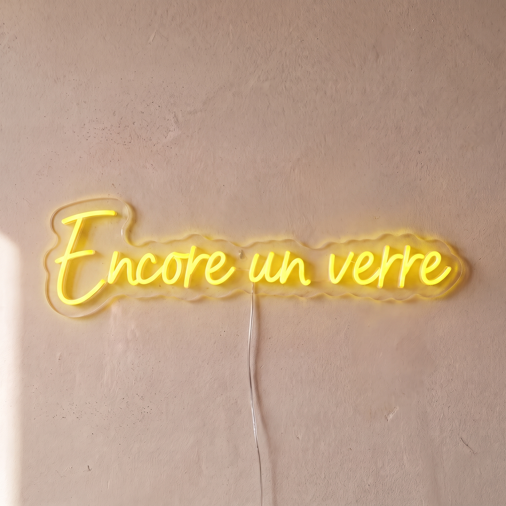 Néon mural « Encore un verre » jaune, gros plan sur fond beige