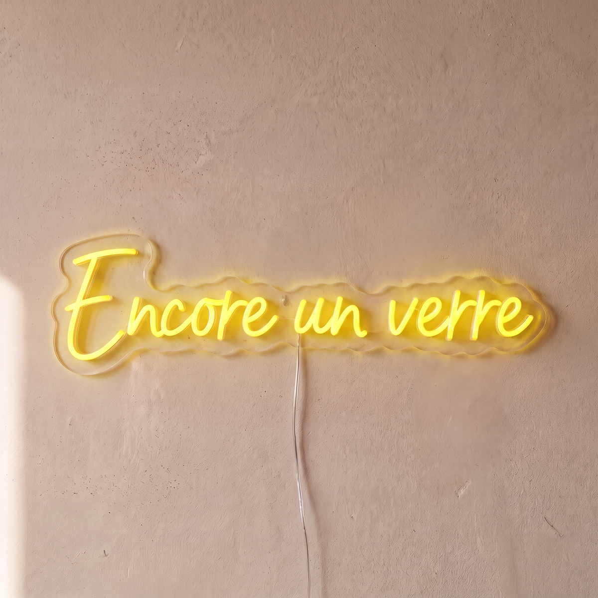 Néon mural « Encore un verre » jaune, gros plan sur fond beige