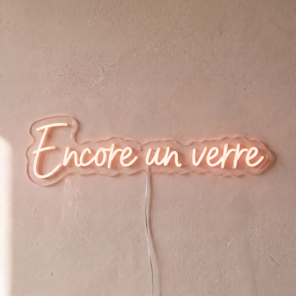 Néon mural « Encore un verre » rose pâle, gros plan sur fond beige