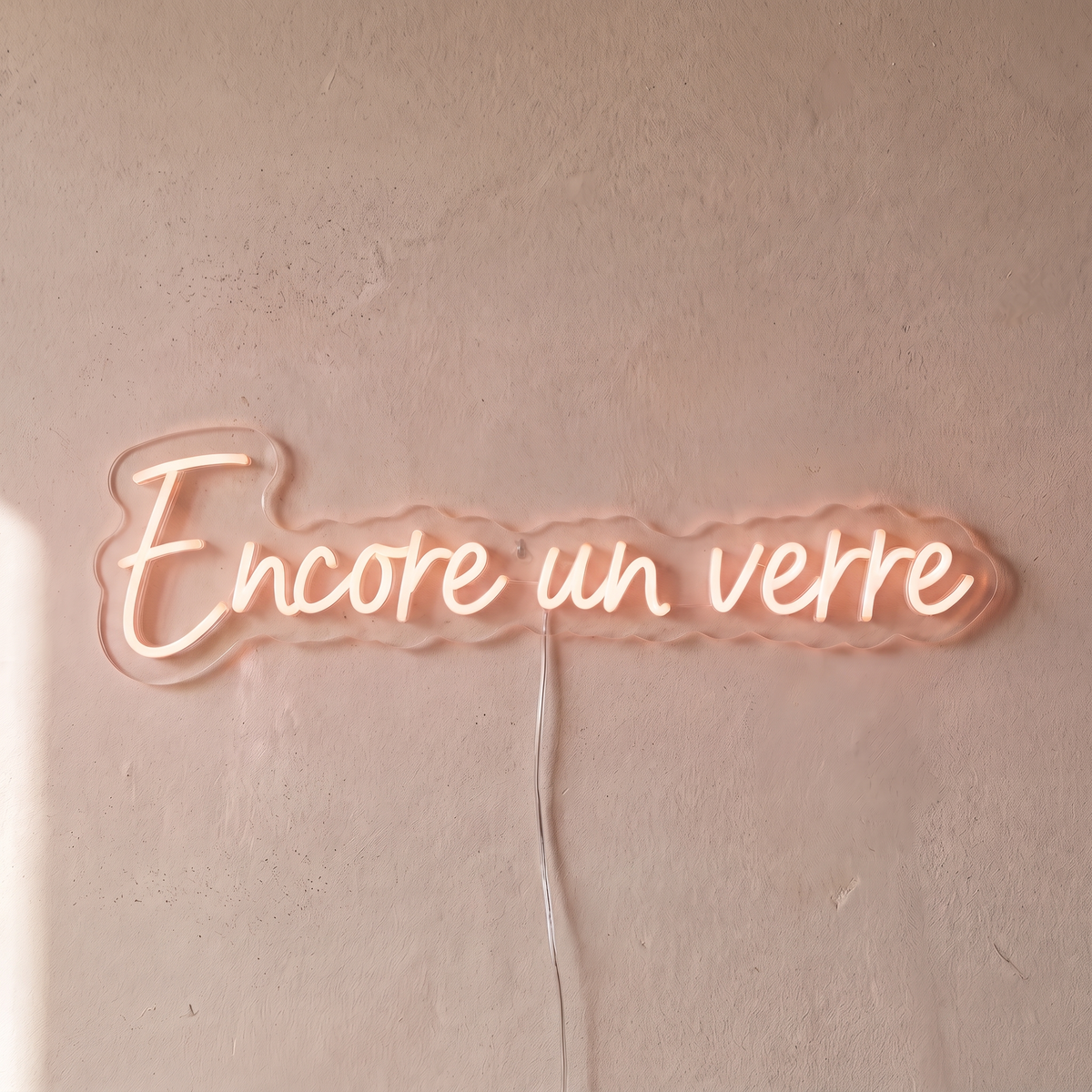 Néon mural « Encore un verre » rose pâle, gros plan sur fond beige