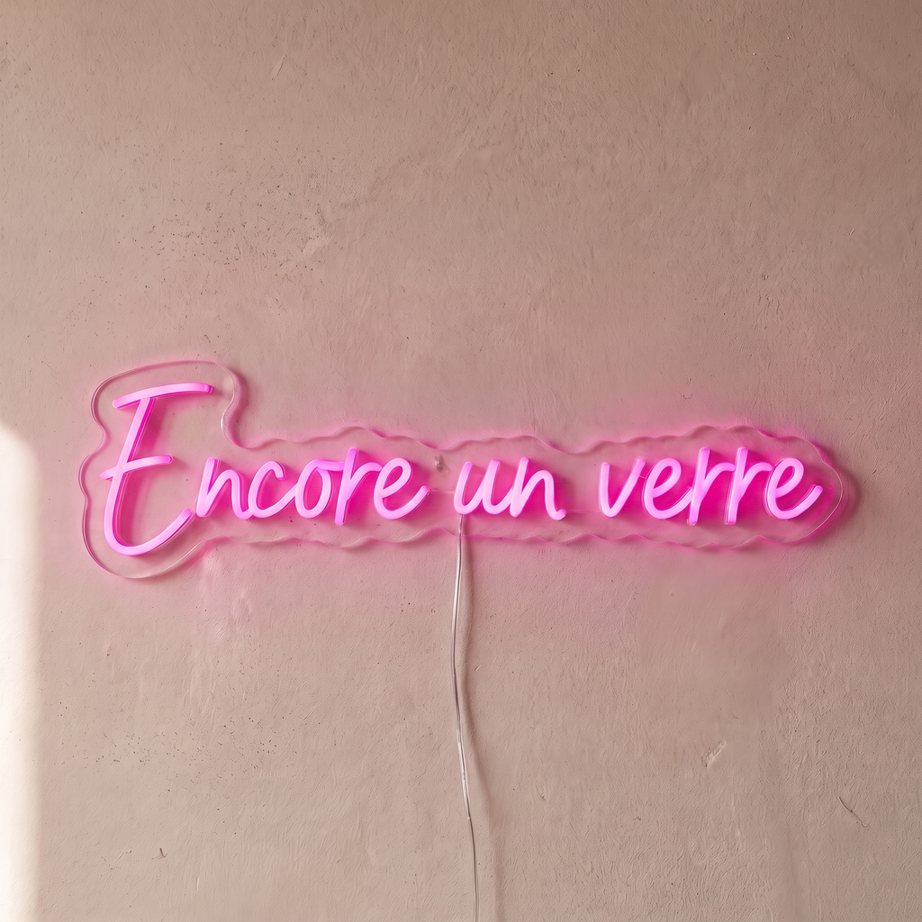 Néon mural « Encore un verre » rose, gros plan sur fond beige