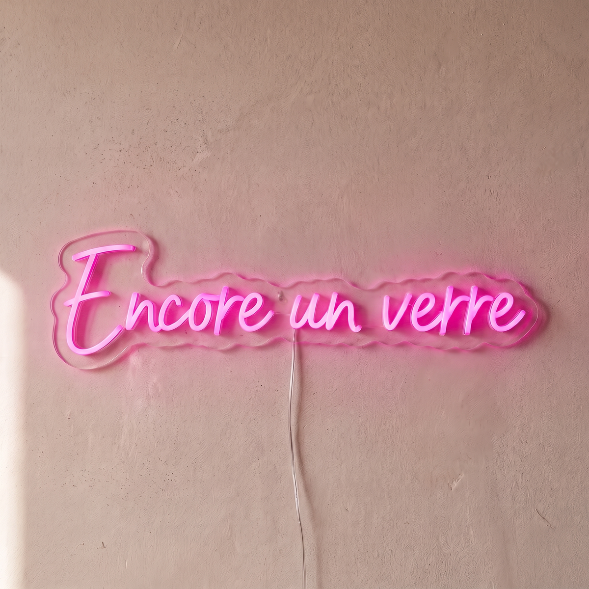 Néon mural « Encore un verre » rose, gros plan sur fond beige