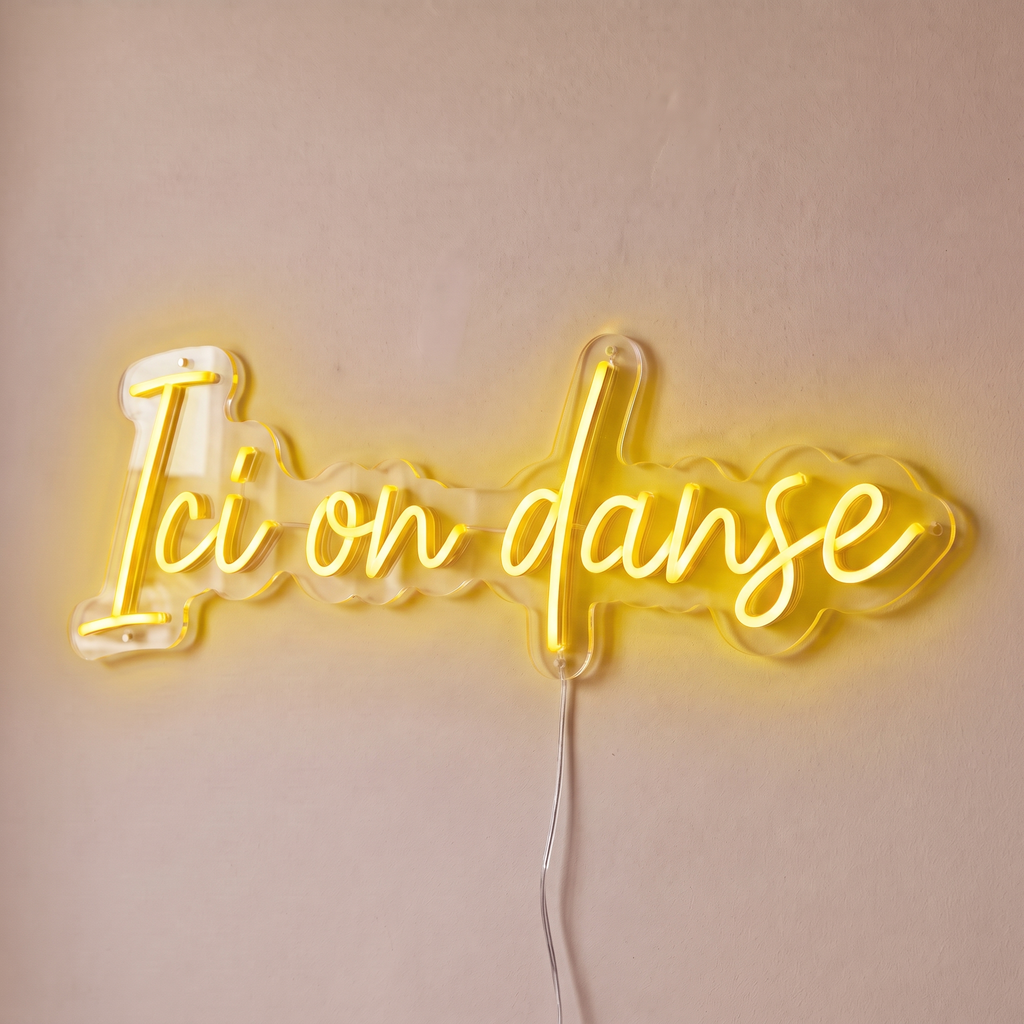 Néon mural « Ici on danse » jaune, gros plan sur fond beige