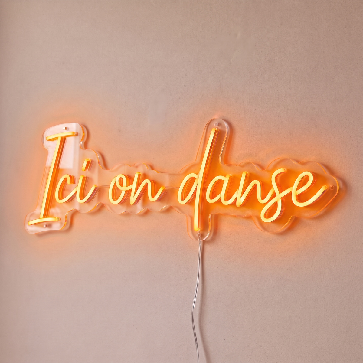 Néon mural « Ici on danse » orange, gros plan sur fond beige