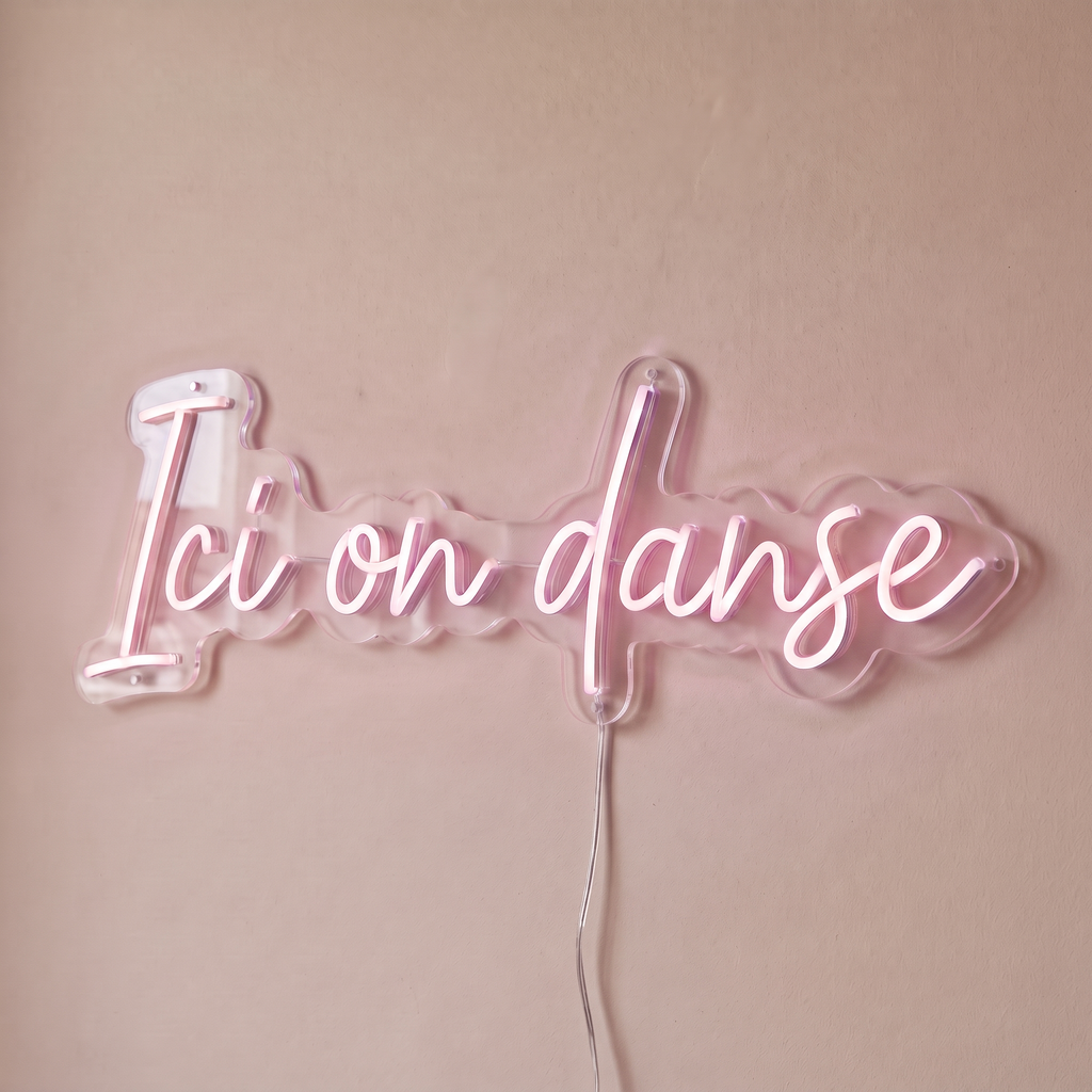 Néon mural « Ici on danse » rose pâle, gros plan sur fond beige
