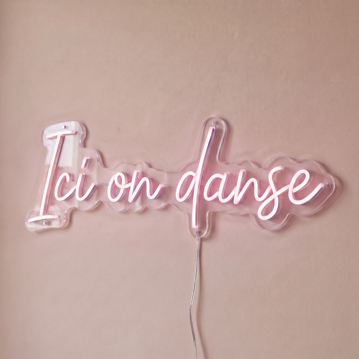 Néon mural « Ici on danse » rose pâle, gros plan sur fond beige