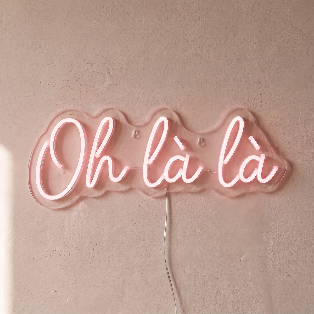 Néon mural « Oh là là » rose pâle, gros plan sur fond beige