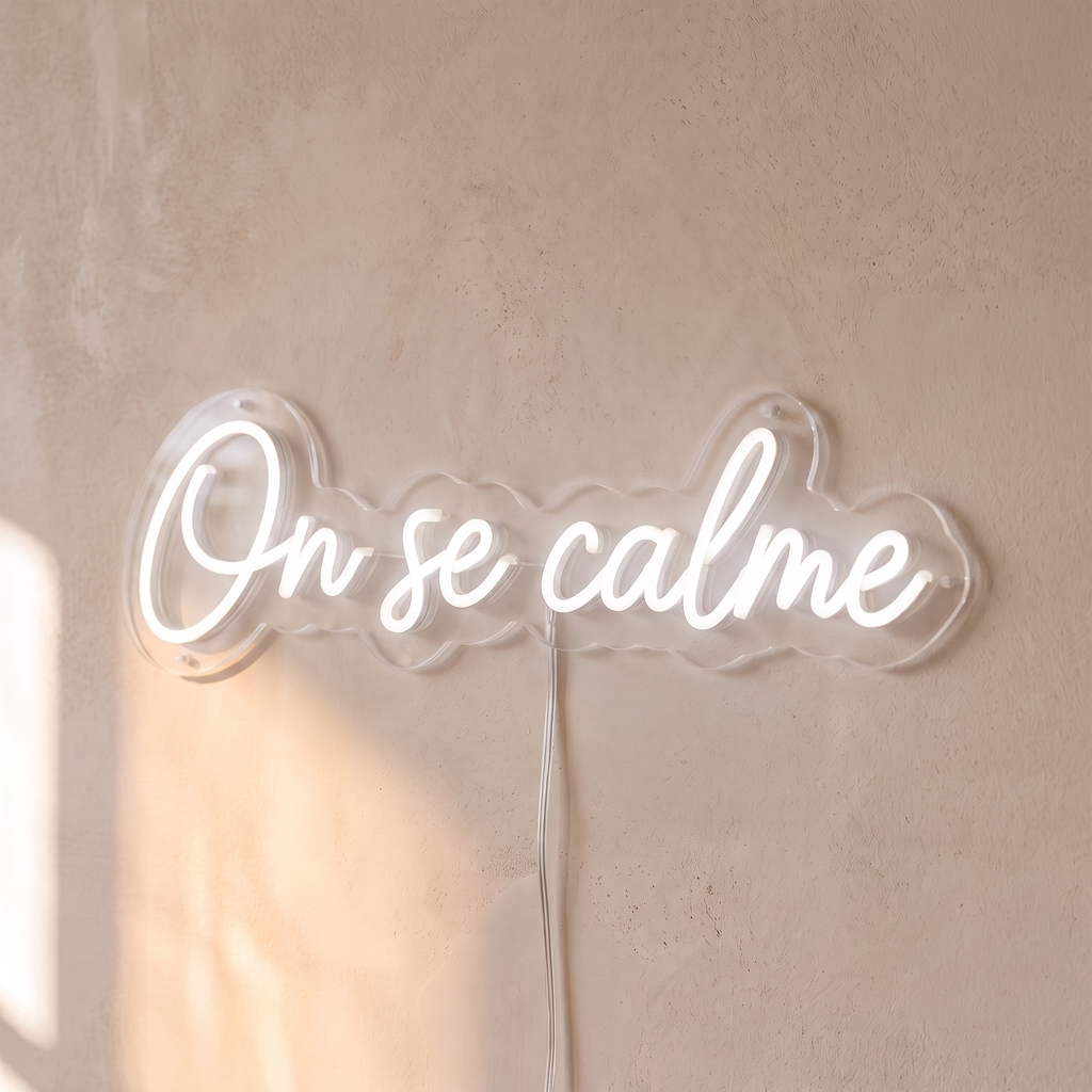 Néon mural « On se calme » blanc, gros plan sur fond beige