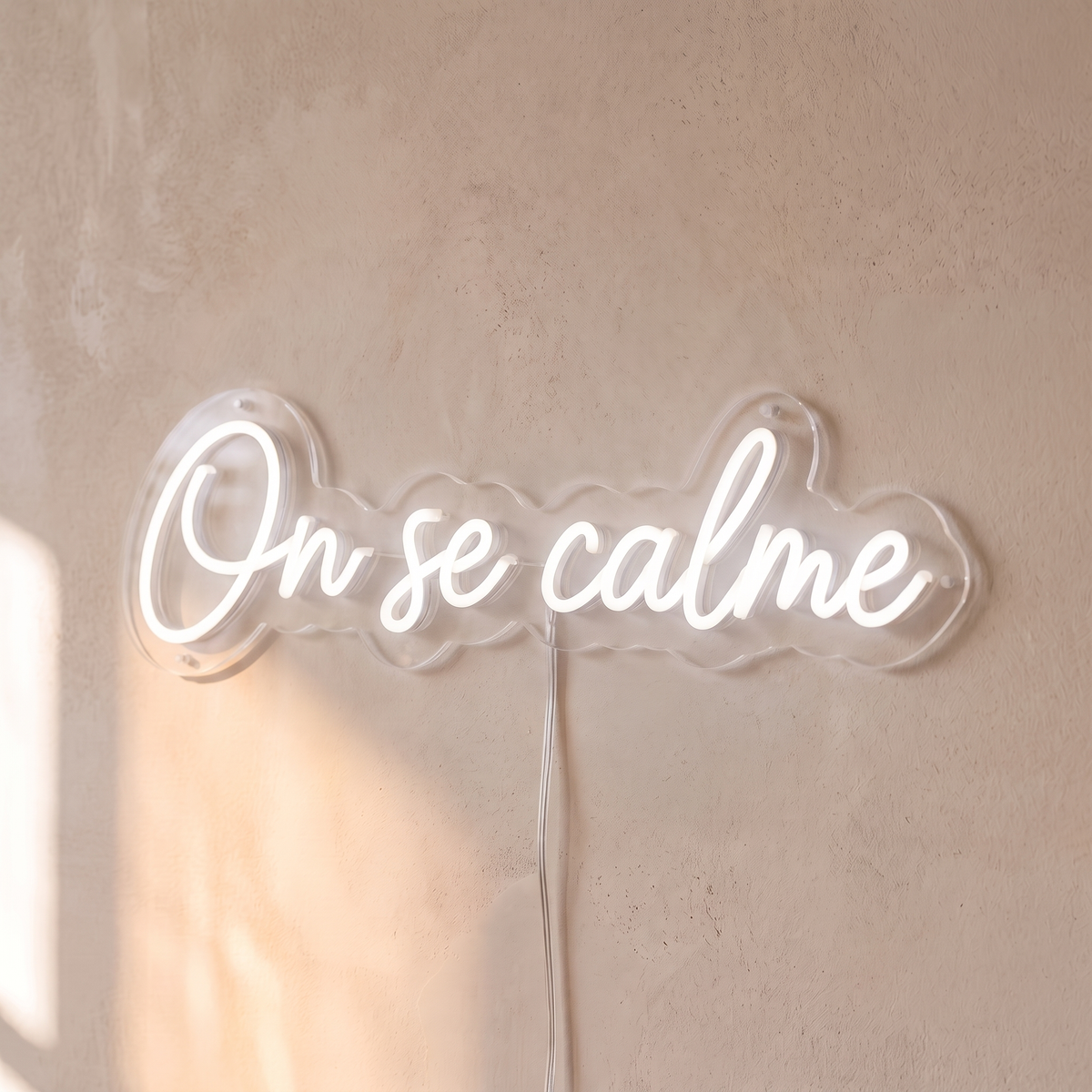 Néon mural « On se calme » blanc, gros plan sur fond beige