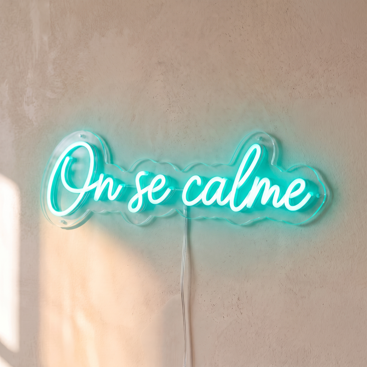 Néon mural « On se calme » turquoise, gros plan sur fond beige