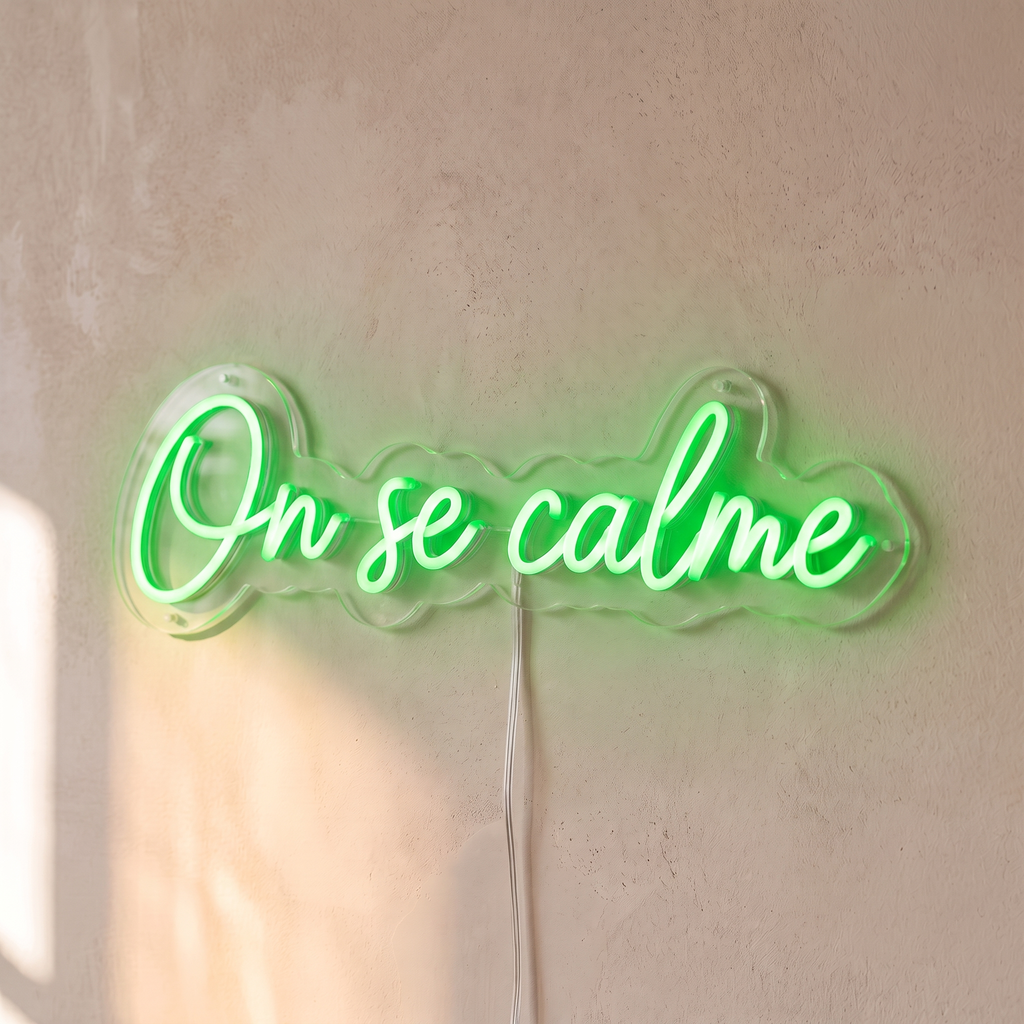 Néon mural « On se calme » vert, gros plan sur fond beige