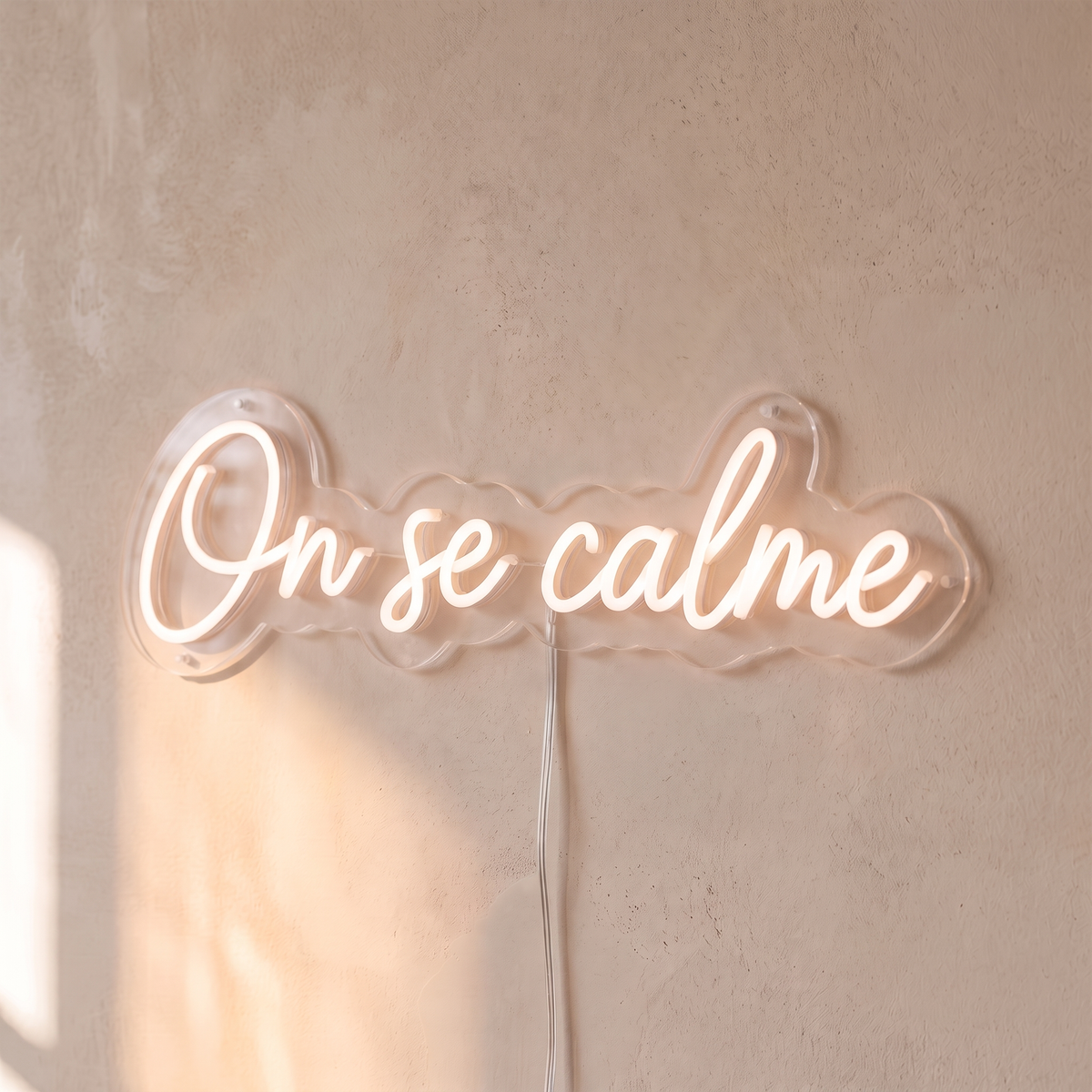Néon mural « On se calme » rose pâle, gros plan sur fond beige