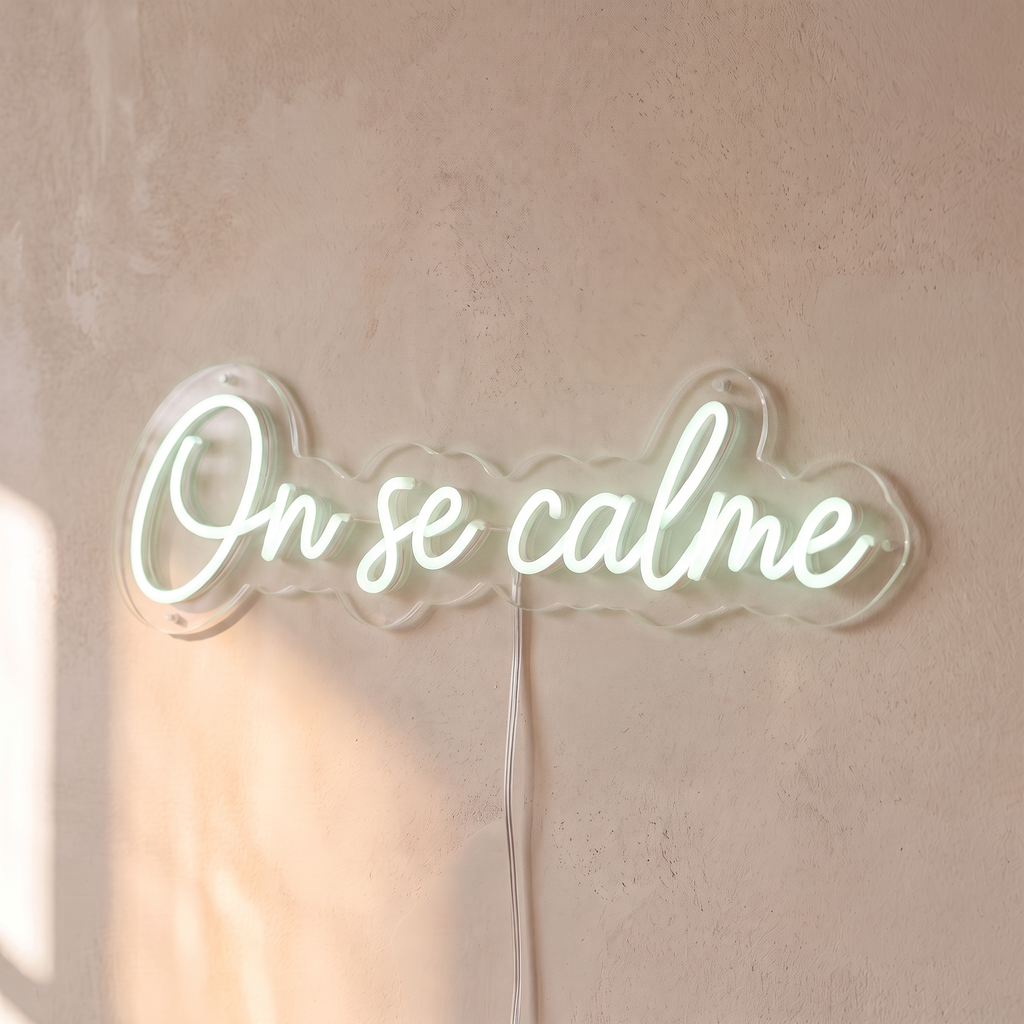 Néon mural « On se calme » blanc froid, gros plan sur fond beige