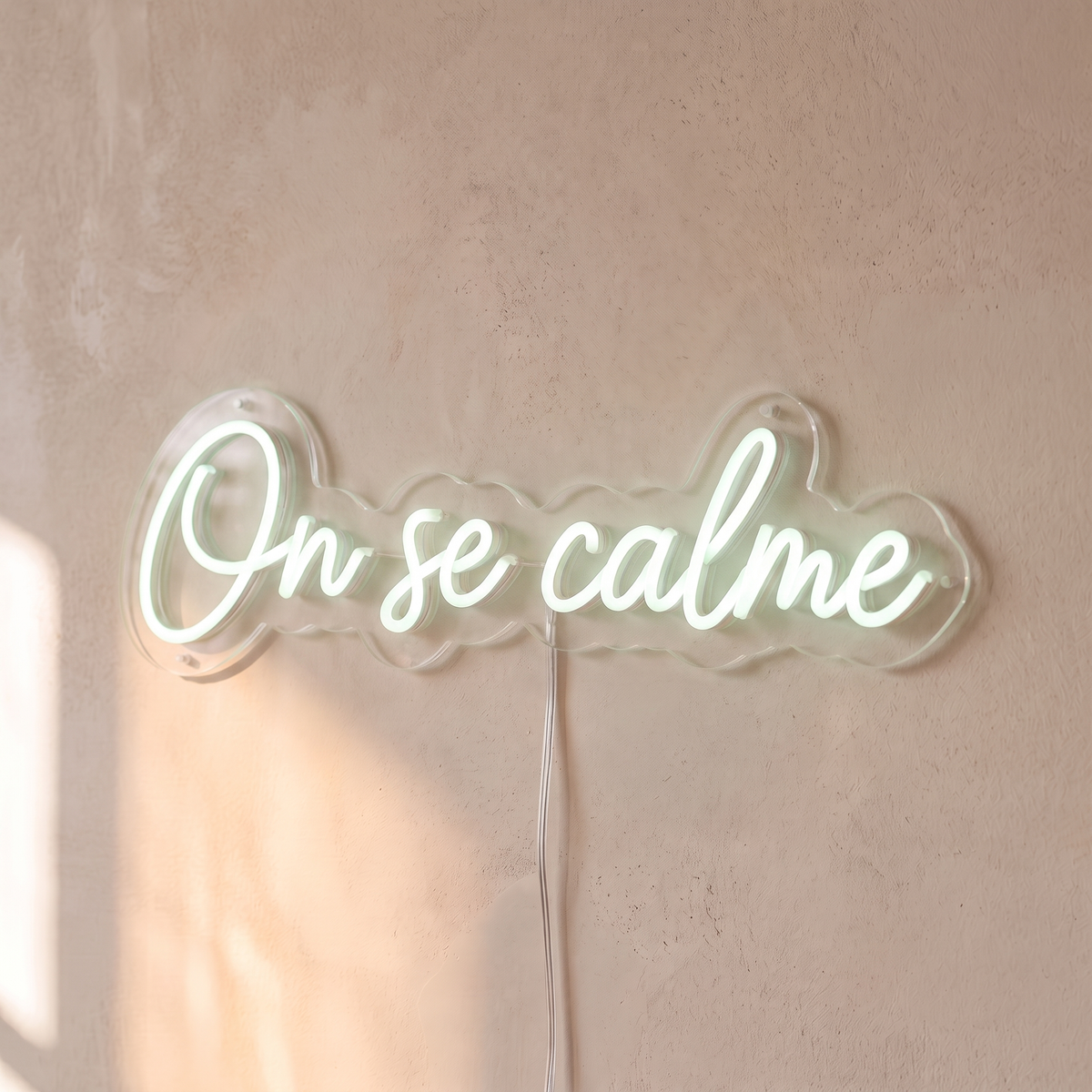 Néon mural « On se calme » blanc froid, gros plan sur fond beige